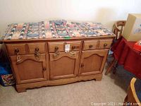 Full front view of wooden maple sideboard with 3 drawers and 3 doors, showing fabric runner on top.