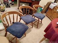 Three maple wooden chairs with gently curved backs and spindle slats, each with a removable blue cushion, arranged on carpet near furniture.