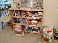 Front view of the faux wood bookcase filled with various books and some decorative items on top.