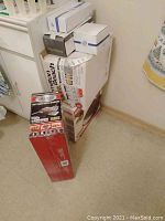 Various boxed kitchen appliances and accessories stacked on floor including Hamilton Beach toaster and George Foreman grill boxes.
