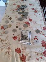 Wide view of coins and novelty currency spread on a floral cloth surface.
