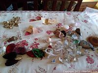 Overview of the lot spread on a floral tablecloth showing crystals, rocks, buttons, paper ephemera, and necklace chain