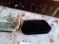 Both purses shown side by side on a floral tablecloth, tapestry purse features countryside scene design and black velvet purse with gold clasp.