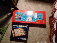 Photo showing two game sets on carpet, Bits and Pieces Sudoku box in front and large red Ez-Fort box behind.
