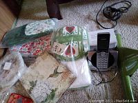 Photo of tea towels, pot holder/oven mitt sets, address book, Easy Threading Needles pack, world dreamcatcher, and VTech phone on the floor.