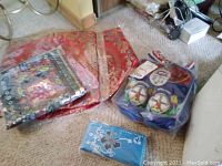 Overview of lot showing pillow shams in plastic bags, slippers in fabric bag, and blue embroidered wallet on carpet.