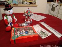 Full lot showing battery-operated snowman, tabletop carousel, boxed and loose ornaments, and decorative lights on red table