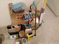 Photo showing assortment of household items including wooden cane, baskets, plant pots, Purex detergent, mop, towel, paint, laser laces, Engrave-It Pro, and Corkcicle tumbler arranged together on floor.