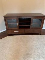 Front view of wooden cabinet showing two glass doors, open shelving in center, and drawers below doors.