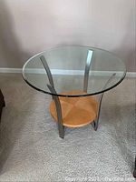 Full view of the round table showing the glass top, metal legs, and wooden shelf.