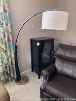 Full view of a modern arc floor lamp positioned near a cabinet and chair, showing the entire lamp structure including base, arm, and shade.