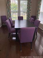 Eight purple upholstered chairs arranged around a dining table in a room.