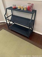 Black metal shelf with three tiers, showing overall structure and placement of items on top shelf.