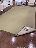 Full view of the large rectangular beige and brown Oriental Weavers area rug laying flat on hardwood flooring with one corner folded to show backing and label.