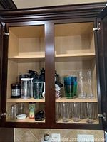 Photo of cabinet interior with assorted glassware, thermoses, and plastic glasses arranged on shelves.