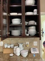 Dishes arranged on open shelves and countertop including mugs, bowls, plates, pitcher, and square side dishes.