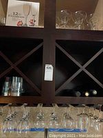 Wine glasses hanging upside down in rack on bottom shelf, champagne flutes in box, other glassware on shelves