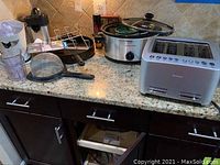 Counter with all kitchen items including the crockpot, toaster, juicers, strainer, and skillet.