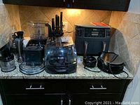 Wide shot of all kitchen appliances on counter including Breville food processor, knife block, Braun immersion mixer, waffle makers, and Ninja Foodi air fryer.