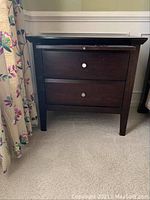 Front view of wooden end table with two drawers and metal knobs, showing overall shape and condition.
