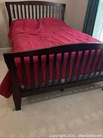 Front view of bedframe with red comforter on carpet floor, showing slatted headboard and footboard.
