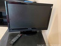 Full frontal view of the Dynex 24 inch TV on stand with remote control placed beside it on a black surface.