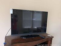 Front view of a 40 inch Dynex flat screen TV placed on wooden furniture with remote control beside it.