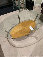 Top view of oval glass top coffee table showing clear glass surface and wooden shelf underneath