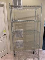 Front view of the metal wire utility shelving unit showing four wire shelves, vertical supports, and wheels at the base.