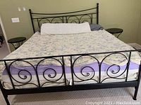 Full view of the black metal bed frame with mattress on it showing decorative swirl design on headboard and footboard.