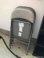 Three padded folding chairs stacked folded against a wall, showing back with fabric upholstery and metal frame with scratches.