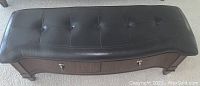 Top view of tufted black leather cushion, showing button detailing and curved edges