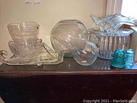 Various clear glass bowls and vases arranged on a dark wooden surface including decorative shapes and two teal salt and pepper shakers.