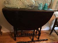 Full view of dark wood drop-leaf table with leaves folded down and one detached leg in front