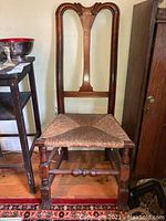 Wooden chair with woven cane seat, turned legs, and decorative carved backrest photographed indoors beside a wooden table and cabinet.