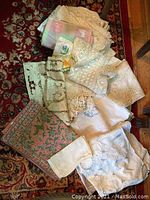 Mixed assorted tablecloths and napkins, various fabric types and colors spread over carpeted floor.