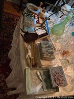 Wide view of table with silver plated swan napkin rings, linen napkins, a whiskey flask, salt and pepper shakers, glassware, and other assorted items on a cream colored draped tablecloth.