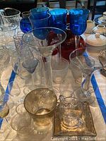 Photo showing various clear glass stemware pieces along with silver metallic glass and other glass items nearby