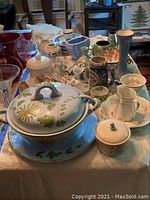 Wide view of the collection on a table showing tureen, plates, cups, vases, and other china items