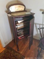 Full view of vintage wooden cabinet, door open showing shelves and stored music sheets inside, arched mirror on top showing loss of silvering.