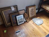 Seven pieces of religious wall art arranged on the floor, including framed prints and a plaster hanging, showing various frame sizes and styles.