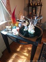Wide shot of all items on a black table showing glass bowl, rabbit figurines, pitcher, paperweights