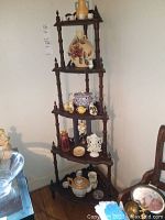 Tall wooden corner shelf unit with five shelves holding multiple decorative items including tea pots, vases, figurines, and small cups.