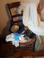 Wide view showing the white antique dress laid over a wooden chair with gloves, spectacles, candle snuffer, and a small mirror on the seat of the chair.