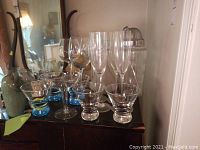 Wide view showing the stemware with blue bases, champagne flutes, frosted decanters, and cocktail shaker arranged on a dark wooden surface.