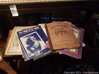 Image showing a collection of vintage piano sheet music with worn covers and varying designs, including one cover with a woman's portrait.