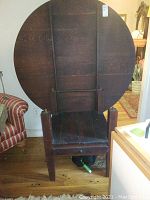 Bottom underside view of the round tabletop, showing the tilt mechanism and attachment hardware. Dark wood with visible grain, some wear and scratches.