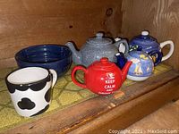 Overview of set including the four teapots, serving bowl, and cow-themed mug on wooden shelf