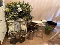 Photo of ceramic and metal planters including rectangular brown, light-colored, green, and scalloped white planters, metal watering can, round wire metal planters, and floral wall hanging decorative piece.
