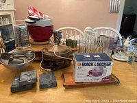 Wide shot showing full collection of kitchenware including mixing bowls, glassware, electric cook pot, Black & Decker chopper box, decorative molds, and metal vegetable cutter on the table.